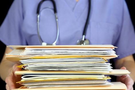 Secretária organizada arquivando pastas de documentos, licenças de funcionamento e notas fiscais no arquivo digital de um consultório médico de alto padrão.