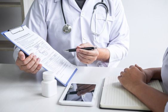 Médico apresentando um termo de consentimento livre e esclarecido (TCLE) impresso para o paciente assinar na mesa do consultório.