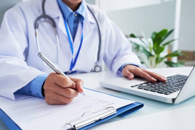 Médico no consultório corrigindo formalmente uma evolução em prontuário eletrônico através de nota de retificação e errata sem apagar o histórico original.